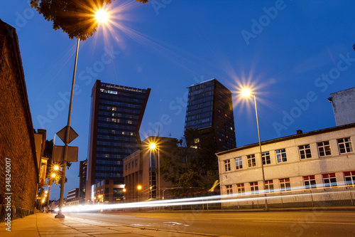 Buildings in night city with lantern. Lithuanian town. Center of Klaipeda. Night life. Empty street with lighted buildings. Deep blue sky in dusk. Skyscraper and historical house. Twilight.Nobody.