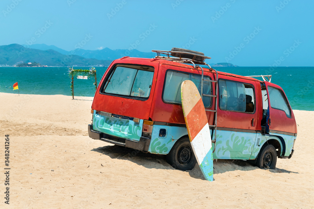 Old bus in the sand and a surfboard on the beach