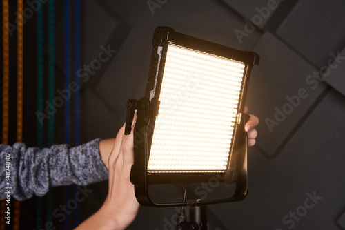 studio assistant fix professional video light on adjustable light stand. Led lamp on tripod in photo studio. Photo and video lamp on embossed grey wall background. photo