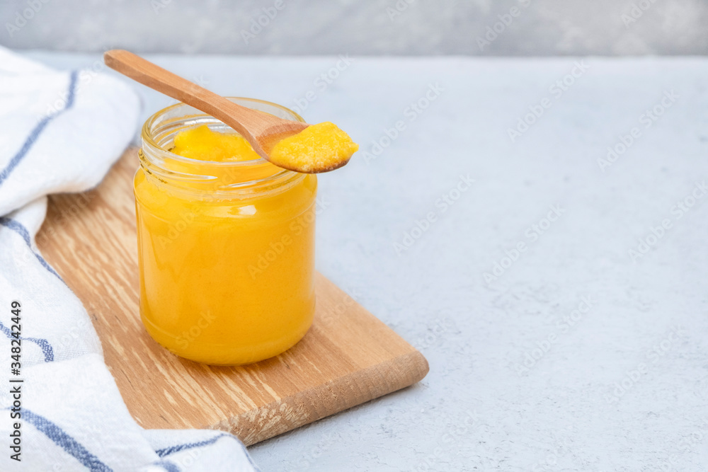 Glass jar of clarified butter (ghee) with wooden spoon on neutral concrete background. Image with copy space Glass jar of clarified butter (ghee) with wooden spoon on neutral concrete background. Image with copy space