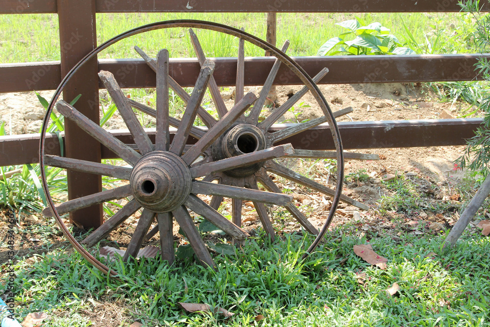 Old cart wheel leaning on a wooden fence.