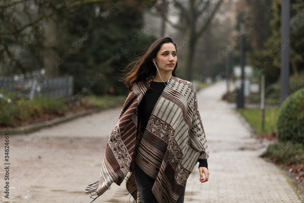 Young Indian woman wearing poncho walking outdoors with head turned looking away.