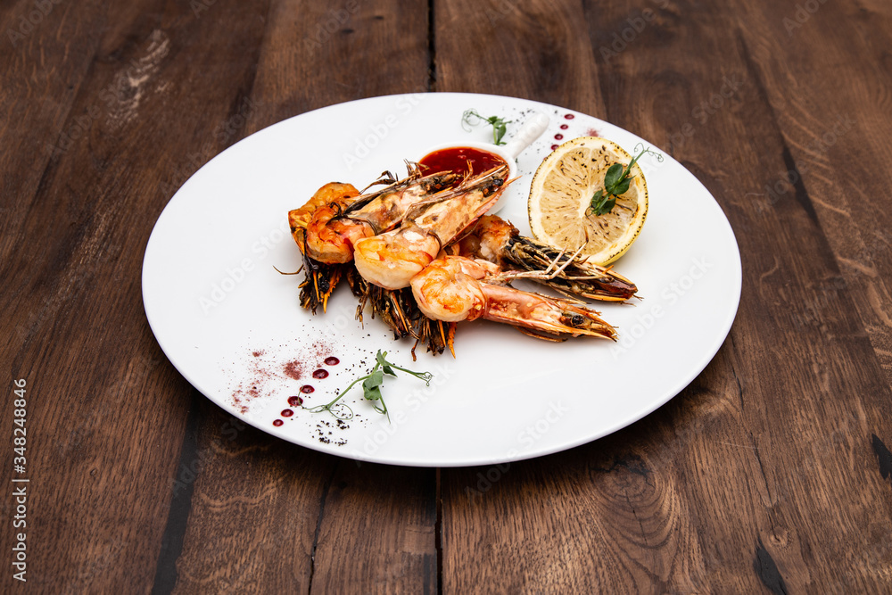 Grilled tiger prawns with garlic, lemon and pepper in Thai sauce in a white plate on a wooden table. Grilled tiger prawns with garlic, lemon and pepper in Thai sauce in a white plate on a wooden table.
