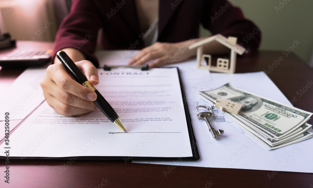 Real Estate Agent's Hand pointing signature Client in Contract Form on table with money, purchase agreement, house key, design home document. Concept of Investment property. Real Estate Agent's Hand pointing signature Client in Contract Form on table with money, purchase agreement, house key, design home document. Concept of Investment property.