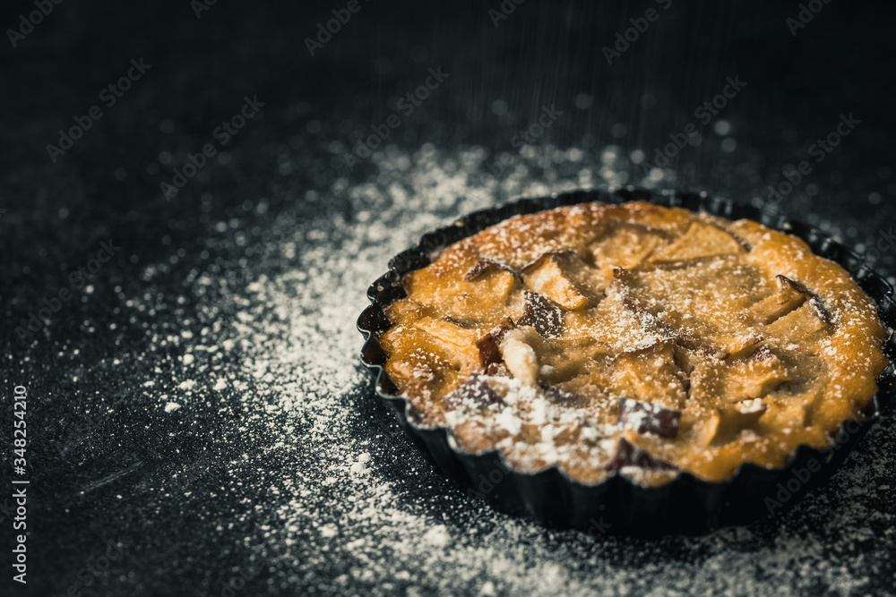Apple tartlet on a black table, sprinkled with powdered sugar. Apple tartlet on a black table, sprinkled with powdered sugar.