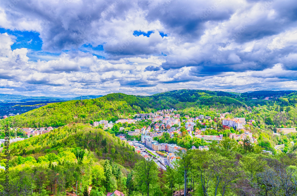 Top aerial panoramic view of Karlovy Vary (Carlsbad) spa town with colorful beautiful buildings, Tepla river and hills of Slavkov Forest with green trees, West Bohemia, Czech Republic