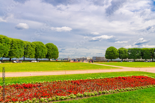 Strelka Arrow of Vasilyevsky Island with flowerbed, benches on green grass lawn and trees in Saint Petersburg (Leningrad) city, cloudy sky background, Russia
