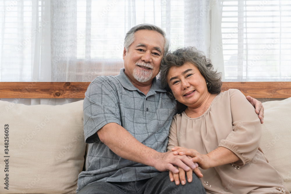 Fototapeta premium Lovely couple Asian elder happy and holding hands sitting together on the sofa at home