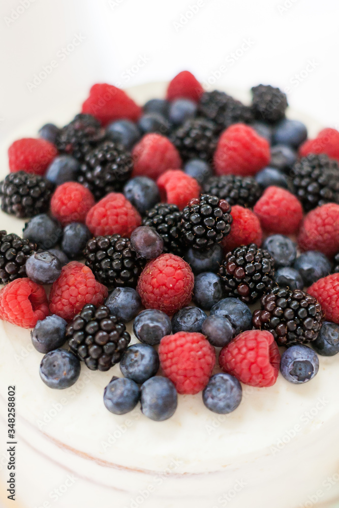 the tip of the white creamy open cake with a mix of wild berries - blueberry, raspberry, mulberry on white table the tip of the white creamy open cake with a mix of wild berries - blueberry, raspberry, mulberry on white table