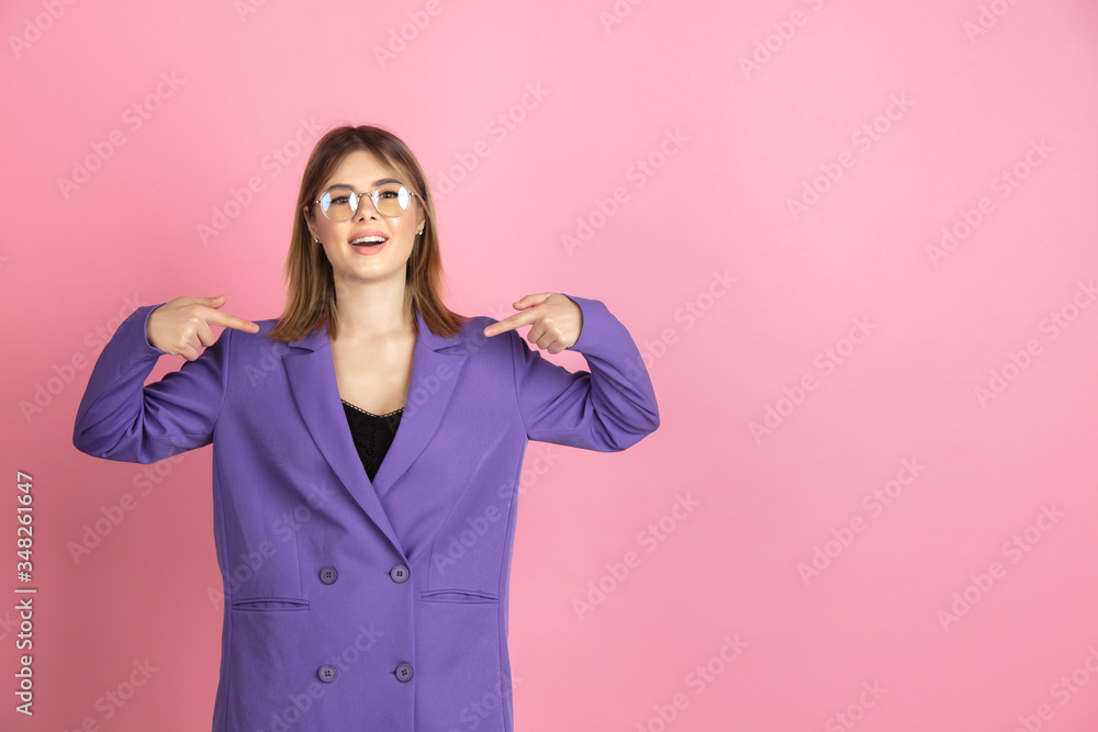Pointing at herself. Caucasian young woman's portrait isolated on pink studio background. Beautiful female model in purple jacket. Concept of human emotions, facial expression, sales, ad. Copyspace. Pointing at herself. Caucasian young woman's portrait isolated on pink studio background. Beautiful female model in purple jacket. Concept of human emotions, facial expression, sales, ad. Copyspace.