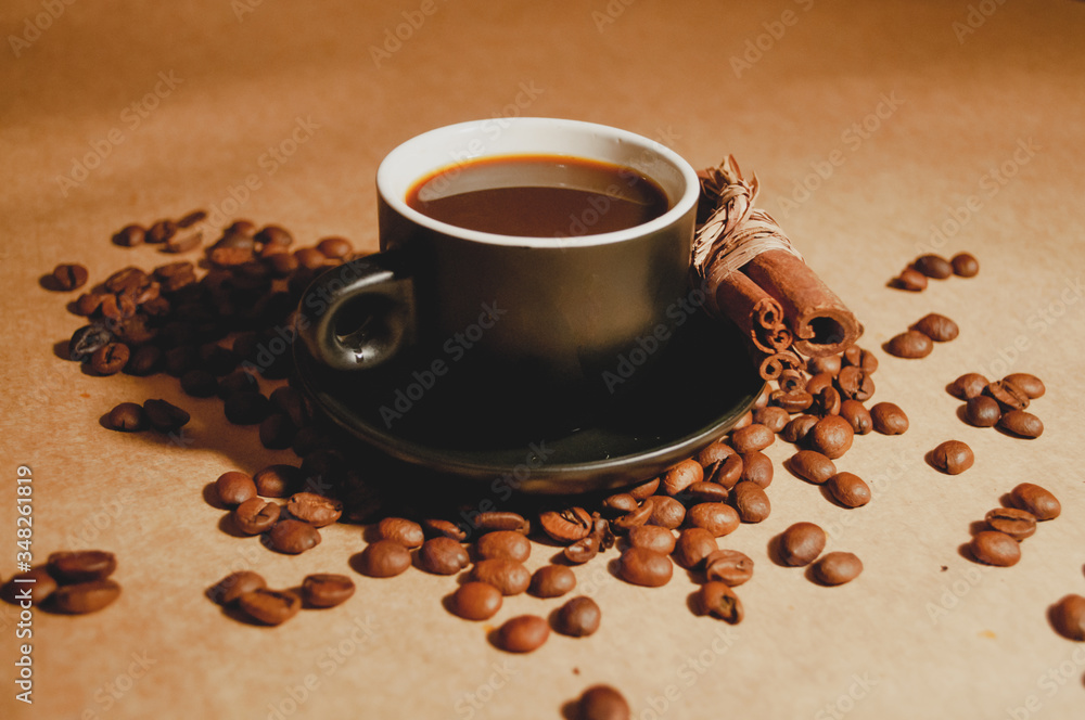 A cup of espresso surrounded by coffee beans and cinnamon A cup of espresso surrounded by coffee beans and cinnamon