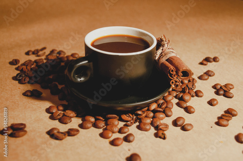 A cup of espresso surrounded by coffee beans and cinnamon