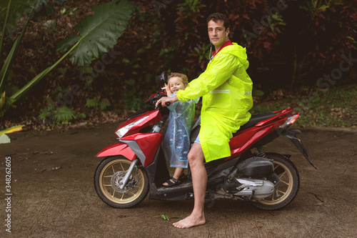 dad with his son on a moped in a tropical growth among palm trees
