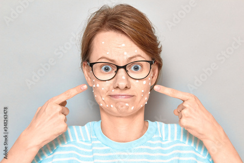 Portrait of cute puzzled girl with white drops of face cream on skin