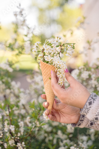Beautiful waffle cone with ice cream decorated with flowers in the girl’s hand with multi-colored bright manicure