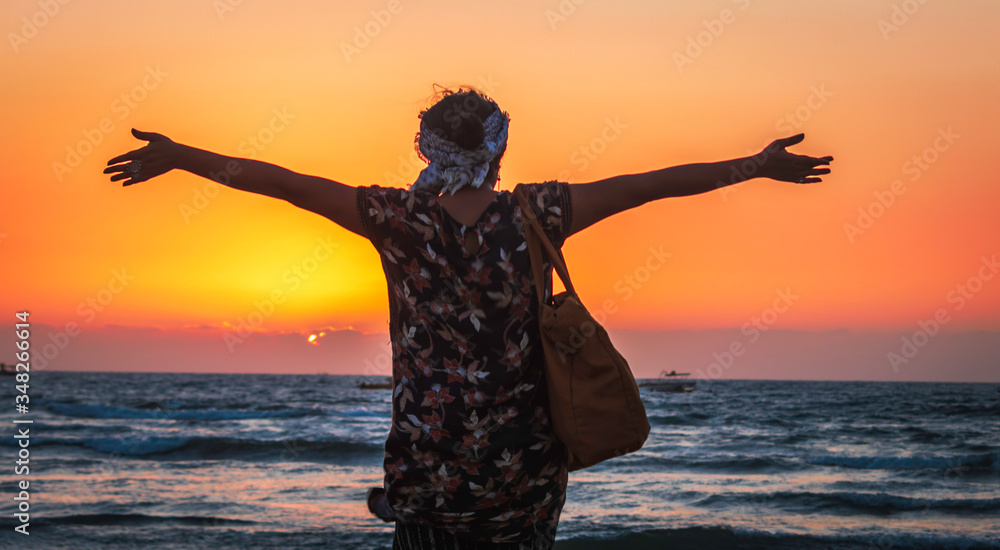 A girl standing on the beach with hands open feeling happy during sunset 