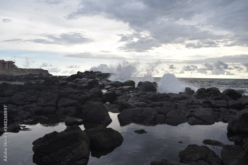 Olas que chocan violentamente contra la costa. El cielo se refleja en el agua entre las negras rocas en un día tranquilo Olas que chocan violentamente contra la costa. El cielo se refleja en el agua entre las negras rocas en un día tranquilo