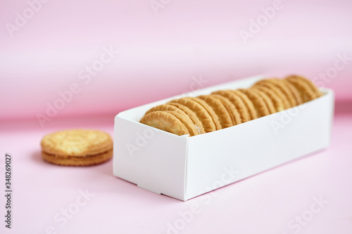 round homemade cookies stacked in a stack in a white box with vanilla cream on a light pink background.