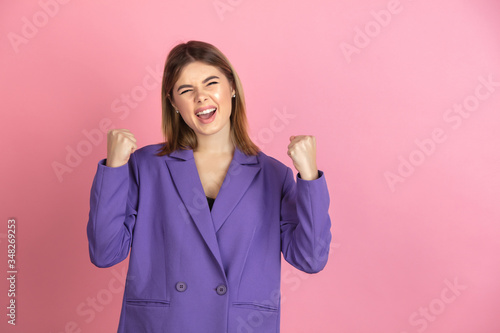 Happy winner. Caucasian young woman s portrait isolated on pink studio background. Beautiful female model in purple jacket. Concept of human emotions  facial expression  sales  ad. Copyspace.
