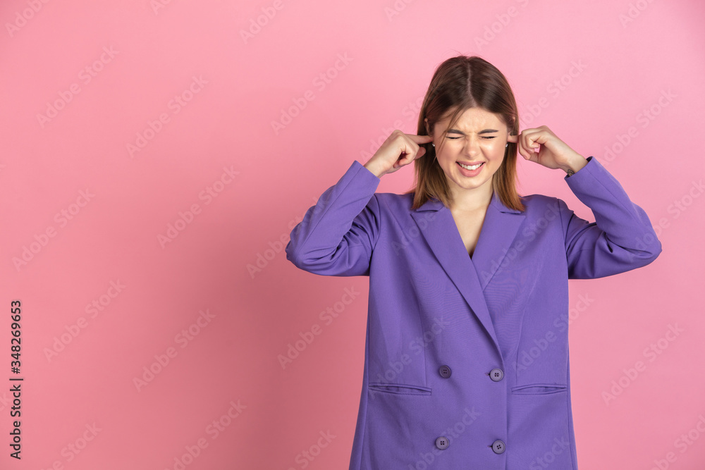 Closing her ears. Caucasian young woman's portrait isolated on pink studio background. Beautiful female model in purple jacket. Concept of human emotions, facial expression, sales, ad. Copyspace. Closing her ears. Caucasian young woman's portrait isolated on pink studio background. Beautiful female model in purple jacket. Concept of human emotions, facial expression, sales, ad. Copyspace.