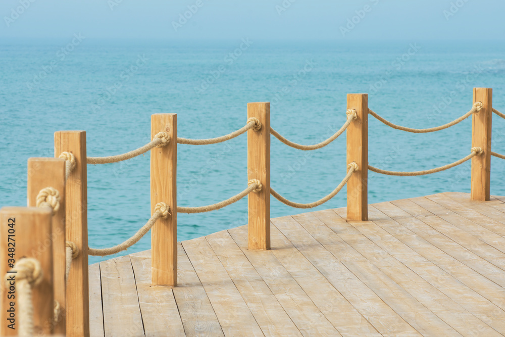 Naklejka premium Wooden platform on the seashore. Wooden poles connected by ropes are placed around the perimeter of the site. Beautiful view of the calm sea.