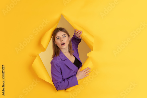 Wondered, shocked. Cheerful caucasian young woman poses in torn yellow paper background, emotional and expressive. Breaking on, breakthrought. Concept of human emotions, facial expression, sales, ad. © master1305