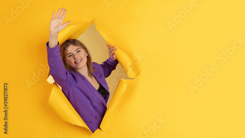 Greeting, showing. Cheerful caucasian young woman poses in torn yellow paper background, emotional and expressive. Breaking on, breakthrought. Concept of human emotions, facial expression, sales, ad. © master1305