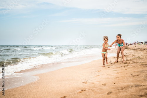 Two positive little girls run along the sandy beach on a sunny warm summer day. The concept of active child rest and children's health. Copyspace