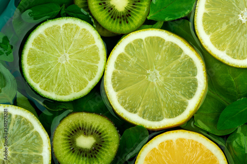 Large flat round slices of different citrus fruits - lime and lemon float together with kiwi and green leaves in water. The concept of tropical freshness 
