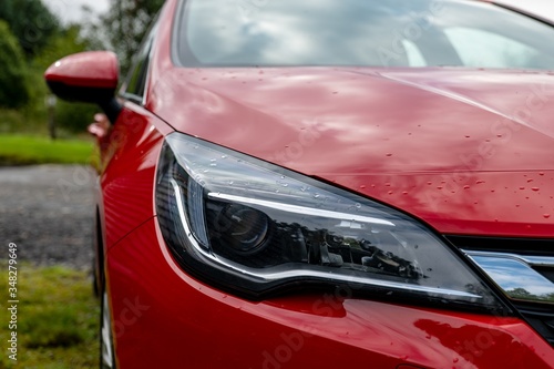 Canvas-taulu Detail of a headlamp and a winker and LED lights of a red modern car with a blur