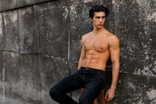 Portrait of a sexy young man with muscular body posing at old black wall. Men's health.