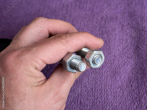 Bolt and nut in male workers hands isolated on purple background