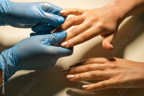 Nail cleaner and hand massage with oil from masseur. Manicurist wearing protective gloves holds hands of the client s with nails polish in manicure salon. Hands close-up. Hygiene and hand care.