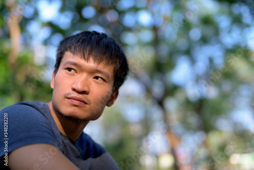 Portrait of young Asian man thinking at the park outdoors