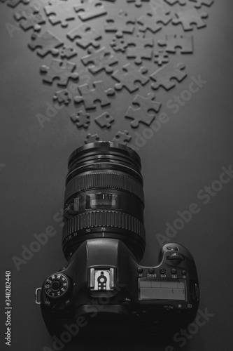 professional camera lies on a black background next to black puzzles that accumulate to the camera lens photo