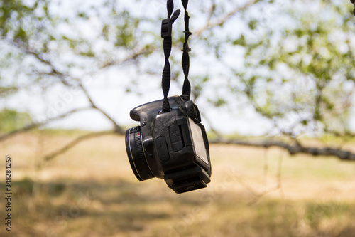  The camera hangs on a tree on a belt on a background of blurry tree branches