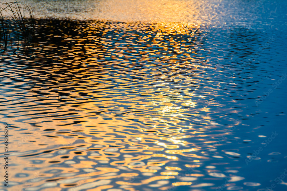 Reflection of the sun in the water. Solar waves. Calm photo of sunset and dawn on the lake, sea, river. Blue and orange waves. Glare and glow. The texture of the water.