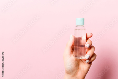 A bottle of cosmetic product in a female hand at pink background with copy space