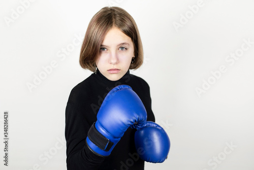 Teenage girl in boxing gloves on a light background. The girl has a serious face because she is preparing for the first competitions in her life © Мар'ян Філь