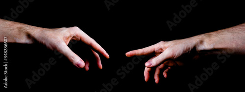 Two male hands trying to touch like a creation of Adam sign isolated on black background. Concept of human relation, community, togetherness, symbolism, culture and history