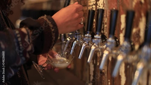 Selective focus of female bartender hands holding and filling glass of alcohol from wine wending machine while standing behind counter in a bar