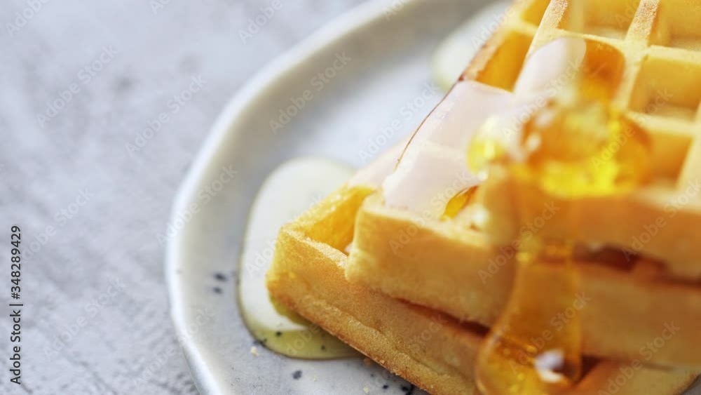 Pouring honey syrup on a crispy waffles in slow motion, close-up. Pouring honey syrup on a crispy waffles in slow motion, close-up.