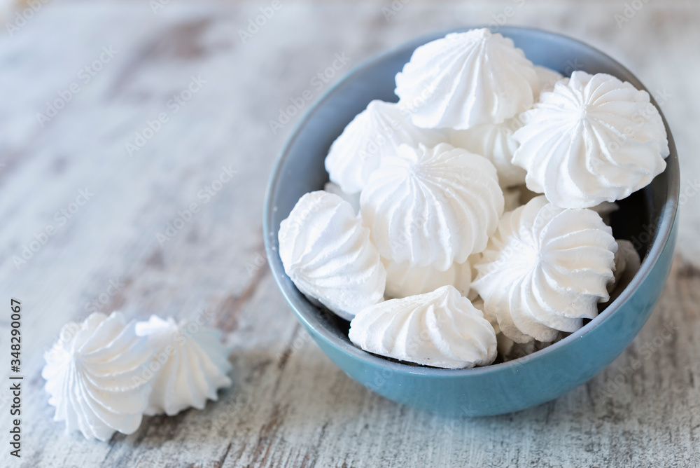 Small white meringues in the blue ceramic bowl and two meringues nearby on the wooden rustic table