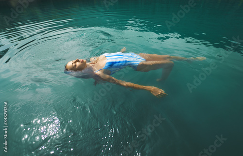 Relaxing woman with eyes closed floating in calm clear water, swimming in blue lake. Outdoor adventure, people in nature and calmness concept