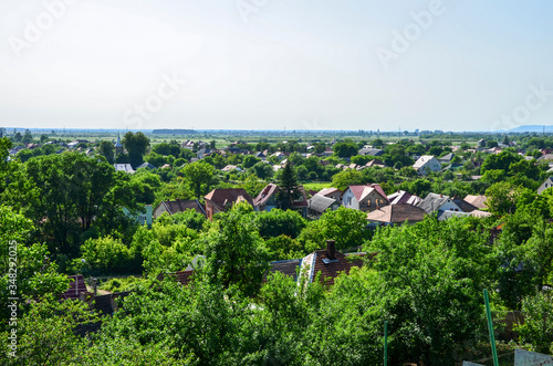 Beautiful view of a typical Ukrainian village in summer with church and houses surrounded by fields green forests under clear sky. Nature background.