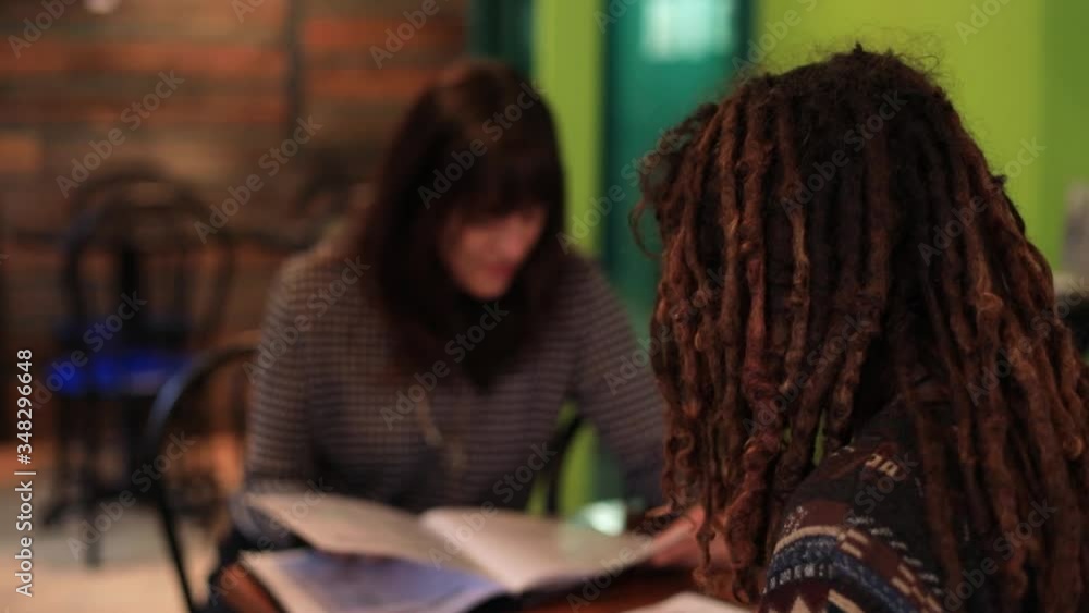 Selective rear view shot of young female friends sitting in modern, restaurant looking at menu book to decide cuisine and food to order for lunch Selective rear view shot of young female friends sitting in modern, restaurant looking at menu book to decide cuisine and food to order for lunch