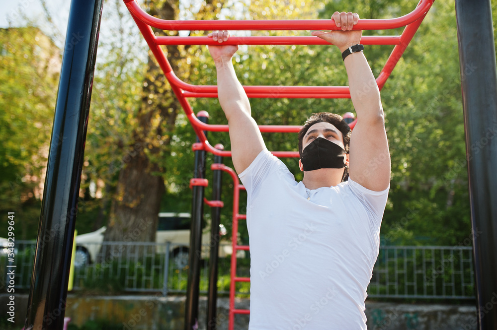 Fototapeta premium Portrait sports arabian man in black medical face mask doing workout exercises in outdoor gym place during coronavirus quarantine.