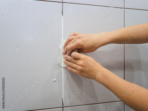 Grouting between tiles in the bathroom. Female hand holds a spatula. Repairs