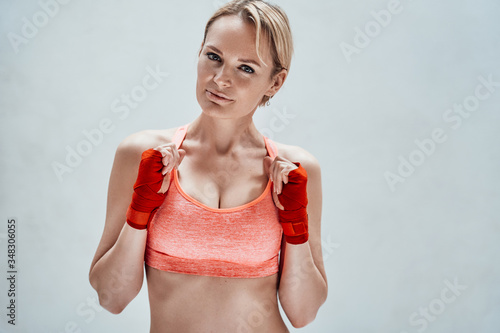 Portrait of a female fitness coach posing in a bright apartment while getting ready for the boxing workout, wearing sporty bra and kumpur tapes photo