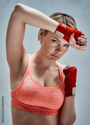 Brave woman with blond hair wearing sportive orange bra and kumpur tapes while covering her face with her hands